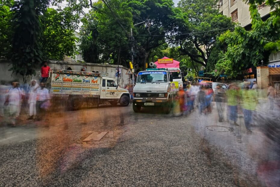 Um Grupo De Pessoas Caminhando Por Uma Rua Ao Lado De Caminhoes PNkzV9KWBT8