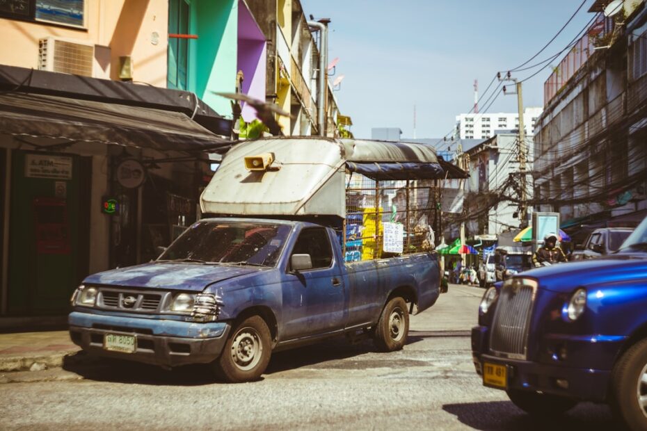 Um Caminhao Azul Dirigindo Por Uma Rua Ao Lado De Predios Altos 0OwaT9BaEeY