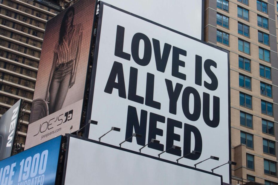 Large city billboard reads 'Love Is All You Need' in New York City street.