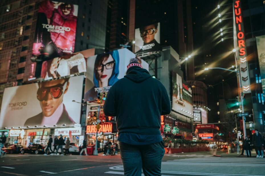 Street scene with a man standing in a vibrant city at night, surrounded by billboards.