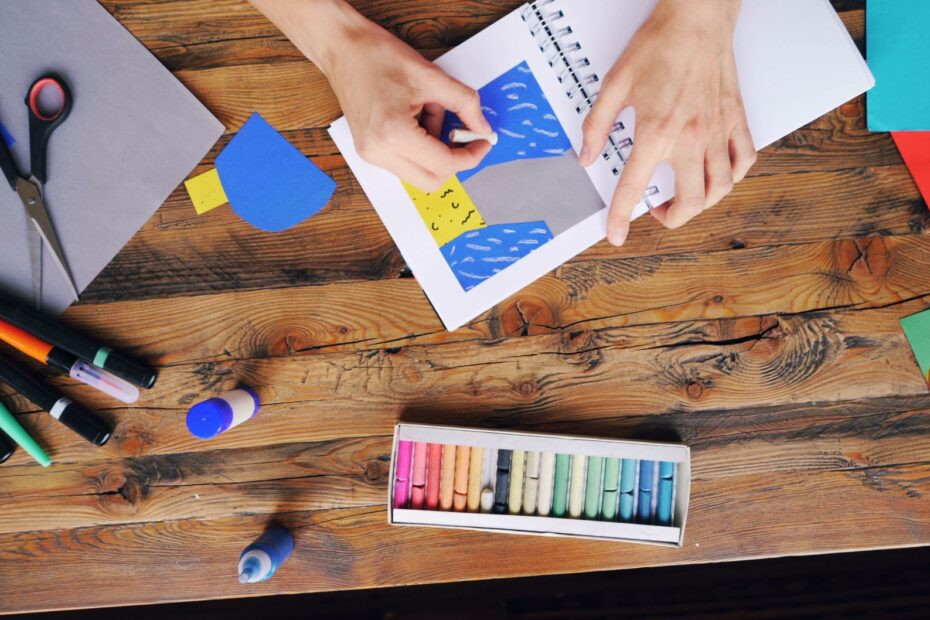 A vibrant arts and crafts setup with colorful papers and pastel colors on a wooden table.