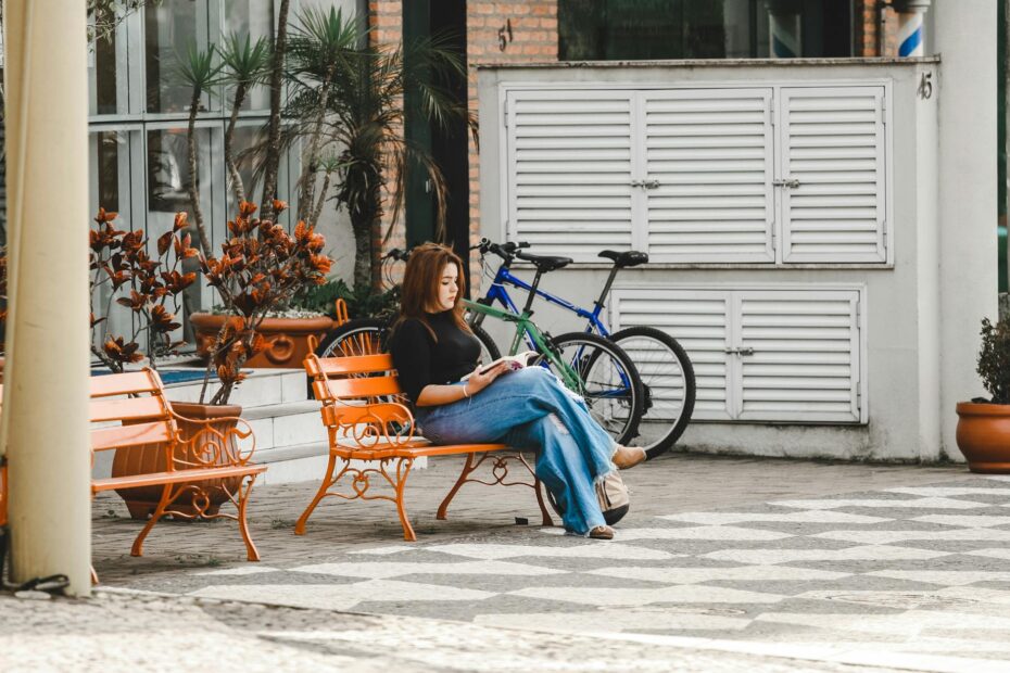 Young woman reading a book on an orange bench outside, enjoying a sunny day.