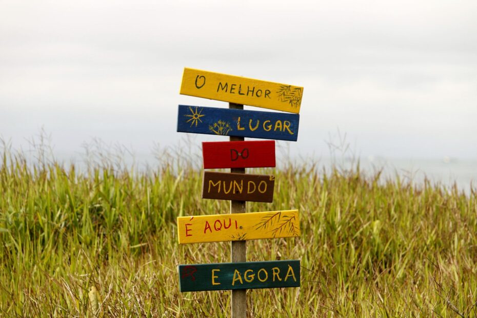 Vibrant multilingual sign in a grassy field in Guaratuba, Paraná, Brazil, showcasing local charm.