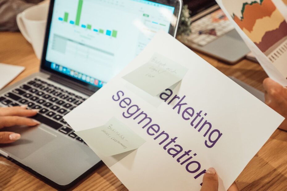 A modern workspace showing hands analyzing marketing data on a laptop and paper documents.
