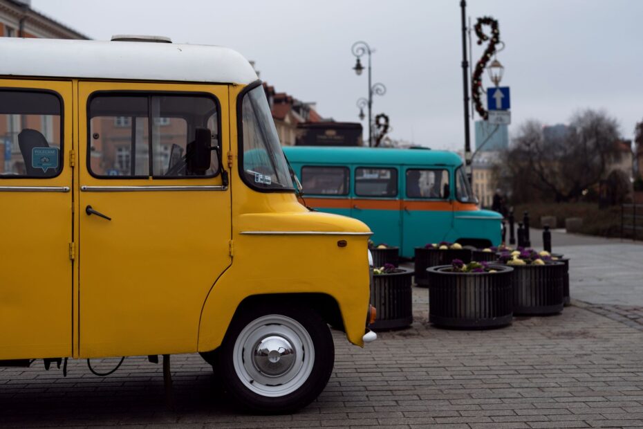 A vintage yellow van parked on a cobblestone street in an urban setting, alongside a turquoise van.