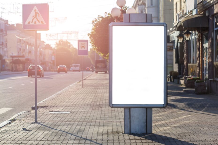 Blank advertisement on tiled walkway with road signs and building in town on sunny day
