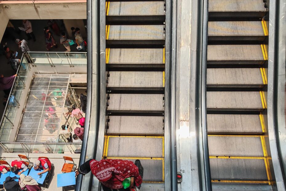 Top-down view of escalators and people in a mall, highlighting busy urban life indoors.