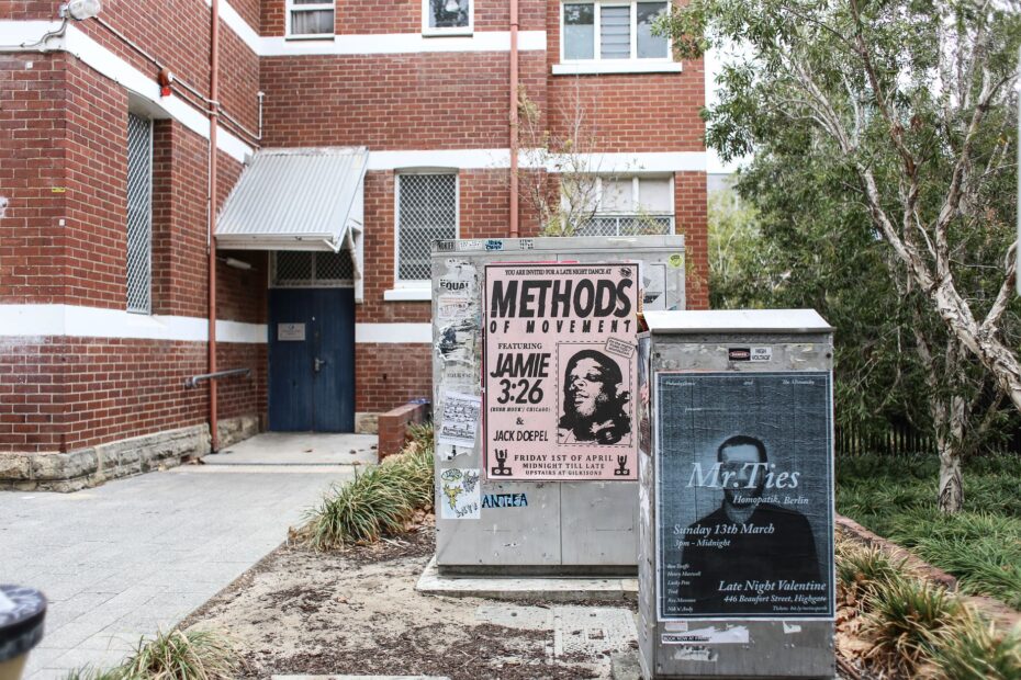 Corner view of a brick building with urban posters and greenery.