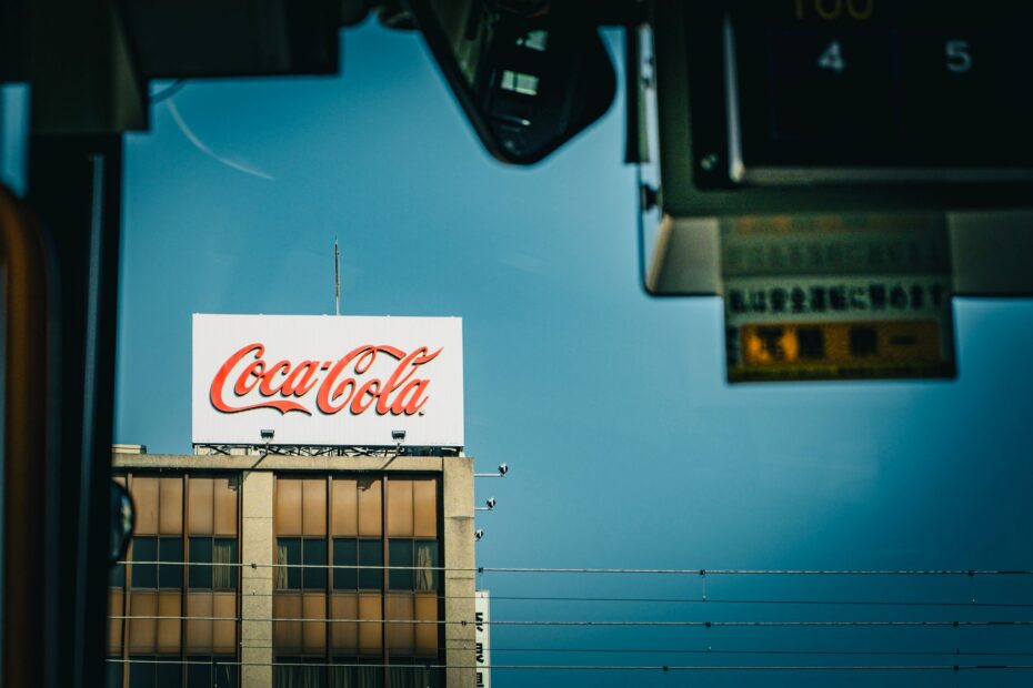 Coca Cola sign atop a building against a clear blue sky, viewed from indoors.