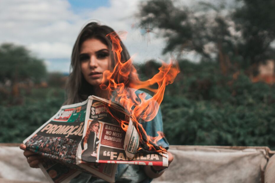 A woman holds a burning newspaper in a dramatic outdoor setting, symbolizing urgency and chaos.