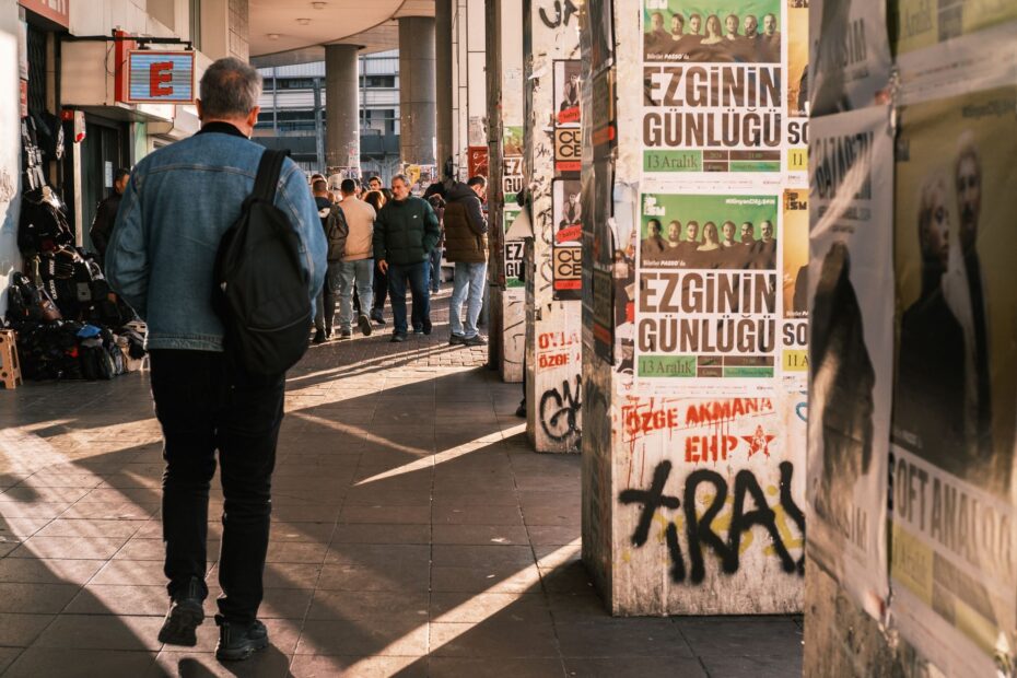 A lively urban street scene featuring pedestrians and poster-covered walls.