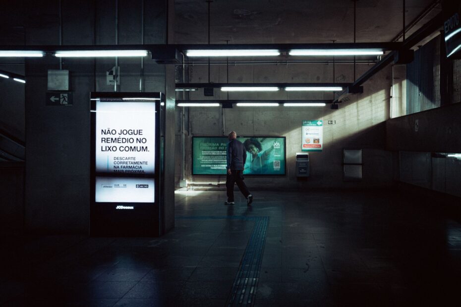 A solitary figure walks through a dimly lit metro station with modern advertising displays.