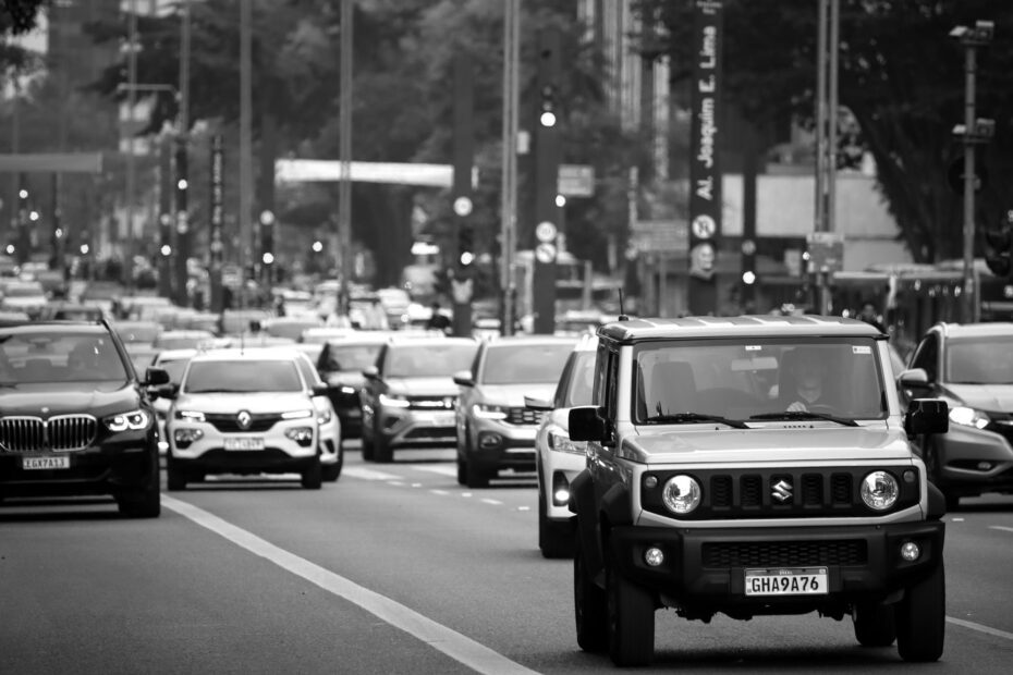 A busy city street scene with various cars in motion, captured in black and white.