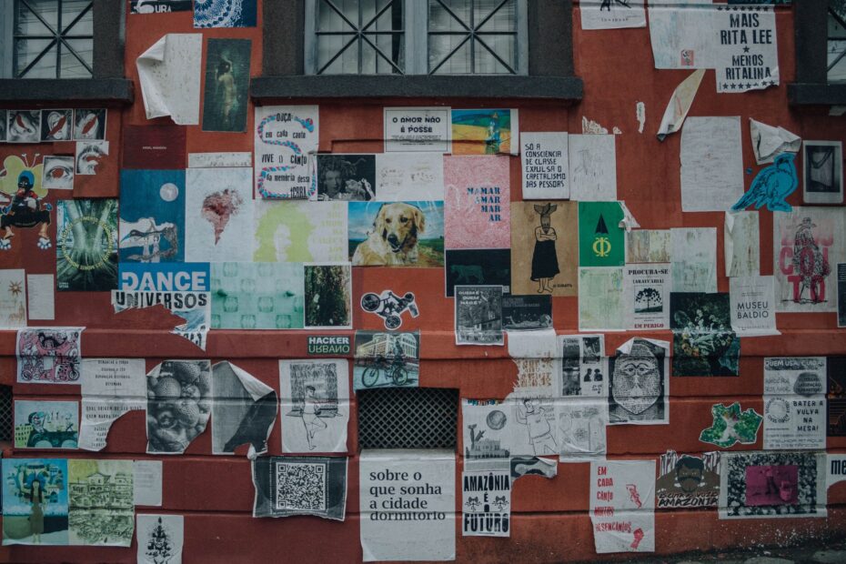 Vibrant street art collage on a red wall, showcasing diverse posters and artistic styles.