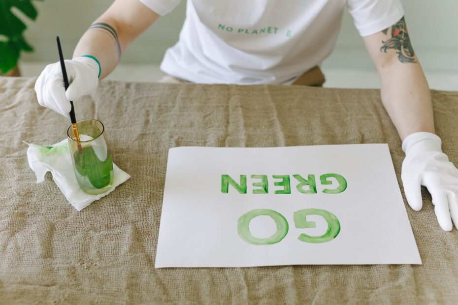 Person painting eco-friendly 'Go Green' message on paper with gloves and brush.